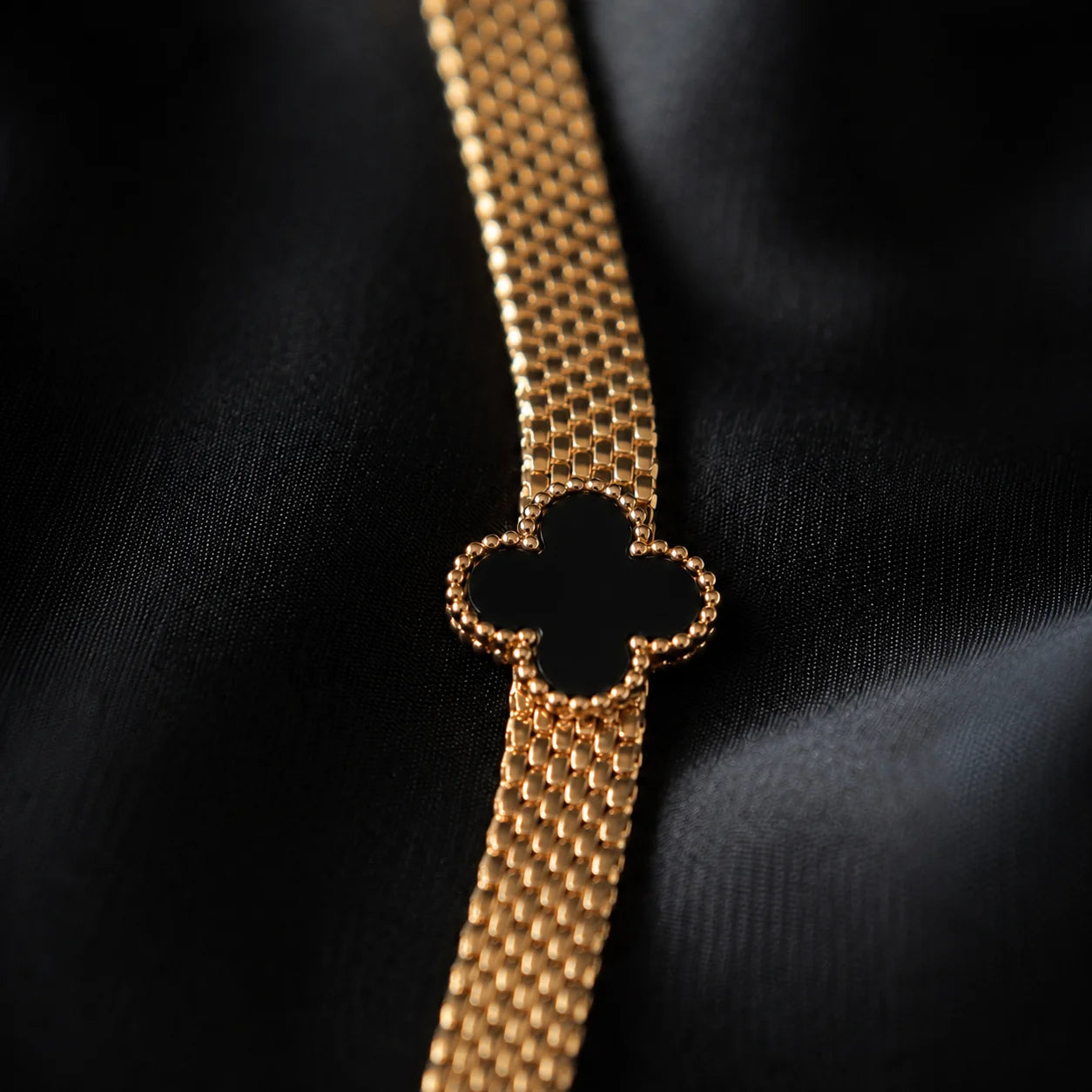 Gold mesh bracelet with black clover centerpiece close-up